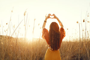 <mujer-en-el-campo-con-manos-en-forma-de-corazon>