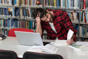 <estresado-joven-estudiante-leyendo-libros-de-texto-mientras-esta-sentado-en-la-biblioteca>