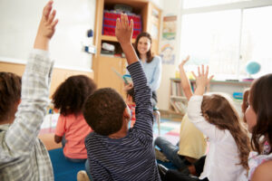 <ninos-de-escuela-primaria-levantando-las-manos-la-vista-trasera-del-maestro>