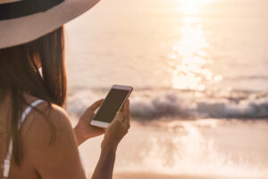 <joven-viajero-con-telefono-movil-en-la-playa-tropical-al-atardecer-vacaciones-y-verano-concepto>
